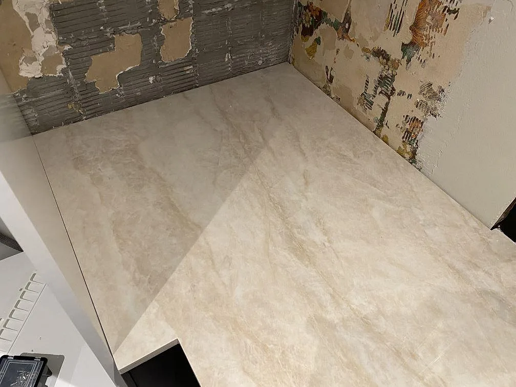 Köksbänk i krämvit Dekton Arga monterad i en hörnsektion mot avbärade väggar, polerad keramik i ett kök i Katrineholm.