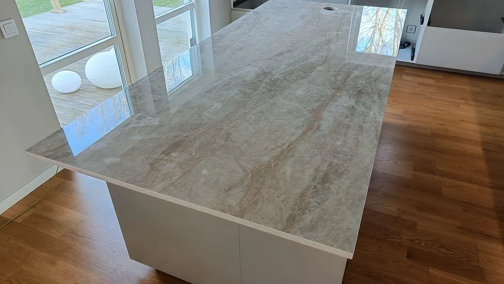 Närbild av polerad köksö i Dekton Arga med beige ådring och stora fönster i köket i Klågerup.