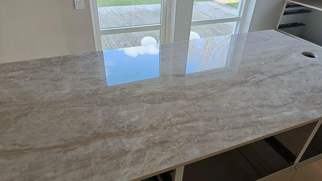 Polerad Dekton Arga som köksö med tydlig ådring, ljusreflexer och vit köksinredning i Klågerup.