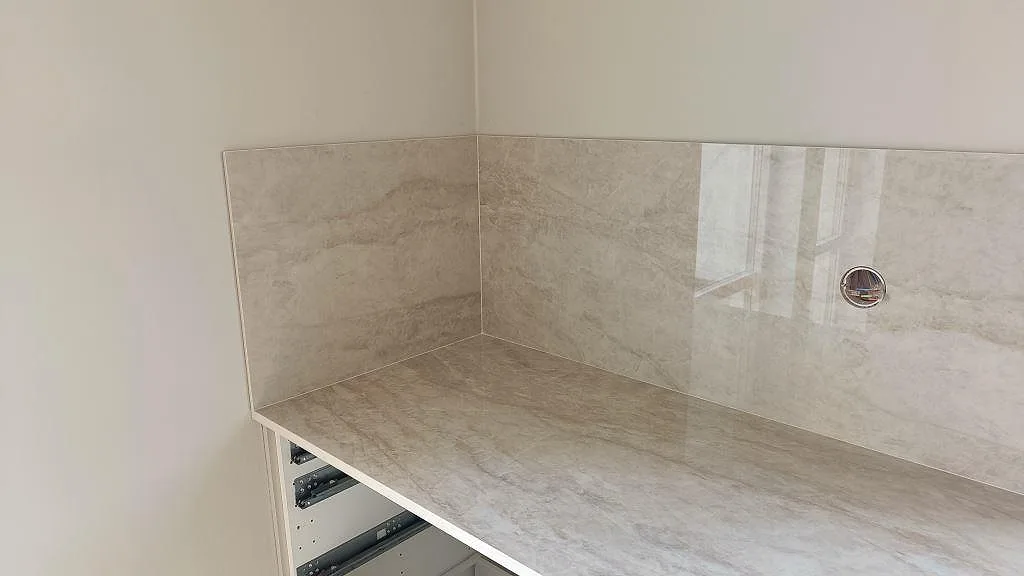 Hörnparti med polerad Dekton Arga som bänkskiva och uppvikt stänkskydd under montering i Klågerup.