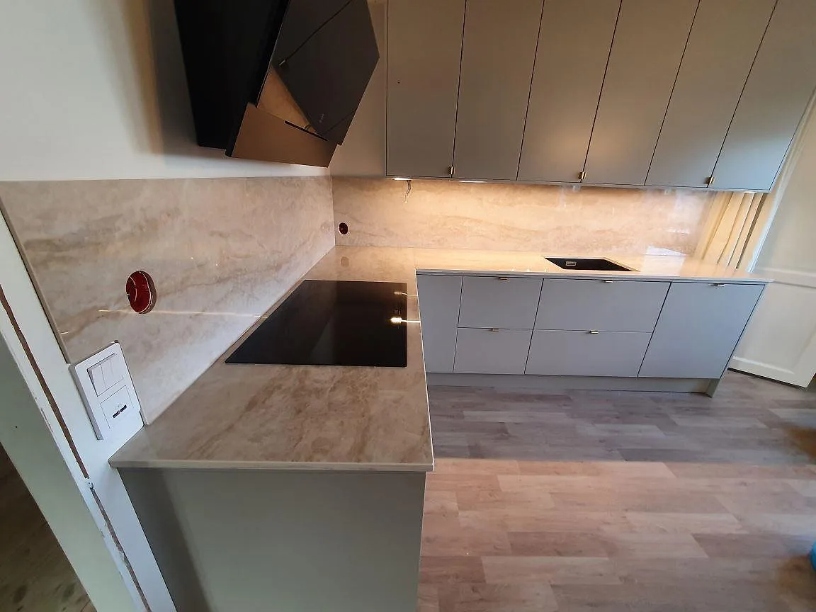Närbild på köksbänkskiva i polerad Dekton Arga med häll och stänkskydd under montering i Knutby.