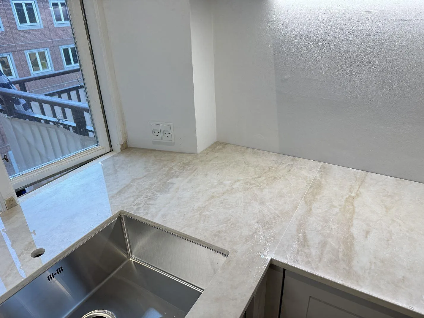Polerad Dekton Arga köksbänkskiva i ljus keramik runt rostfri diskho och blandarhål vid fönster i København N.