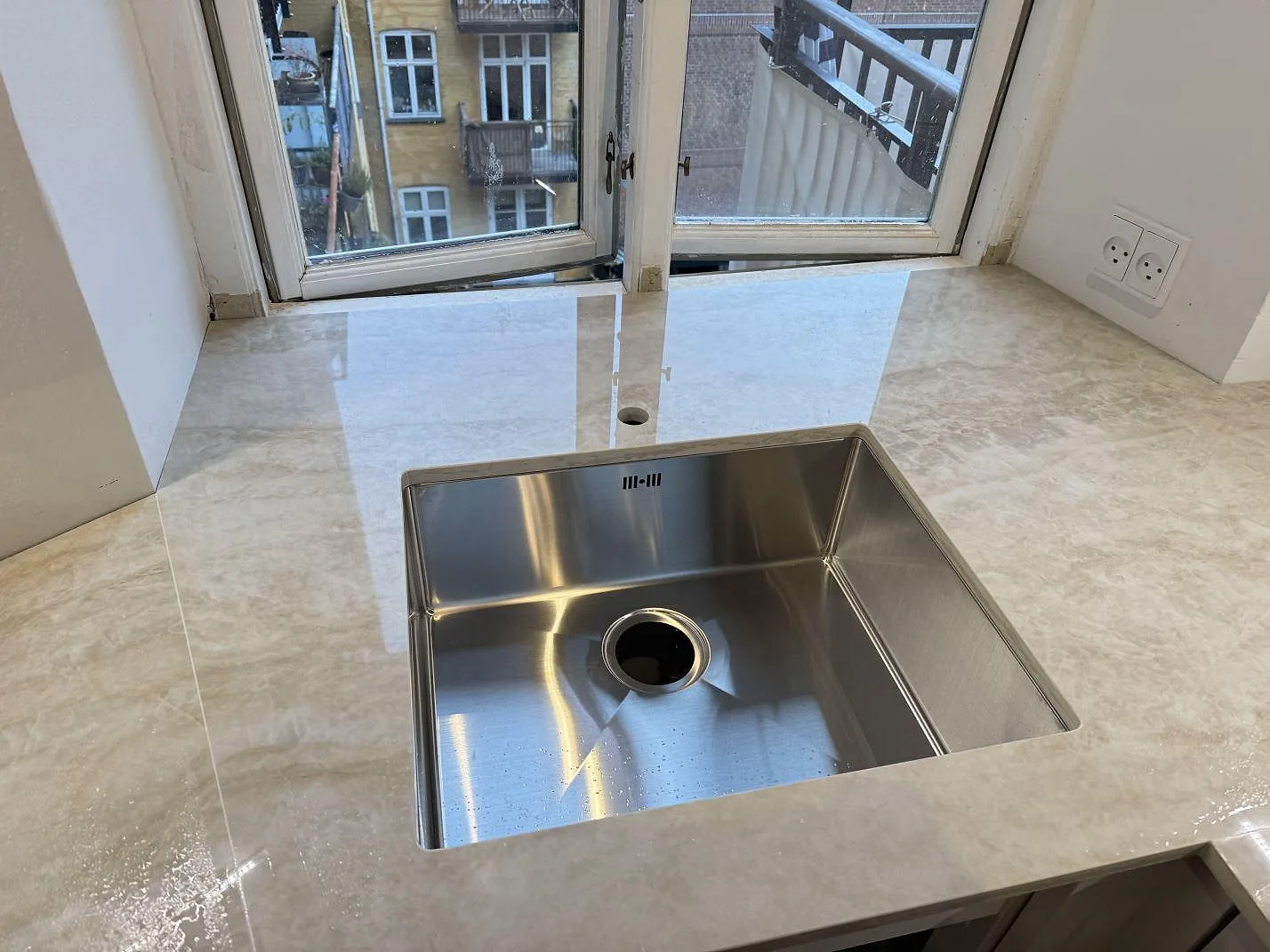 Rostfri diskho i polerad Dekton Arga bänkskiva med blank reflektion och borrat blandarhål i ett kök i København N.