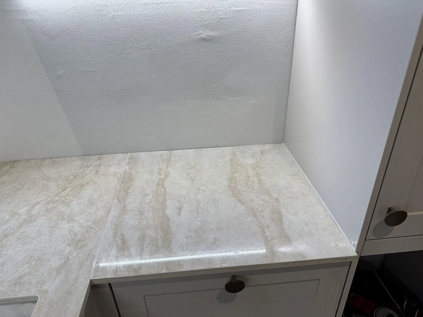 Hörn av L-formad köksbänkskiva i polerad Dekton Arga med varm ådring och grå vägg i København N.
