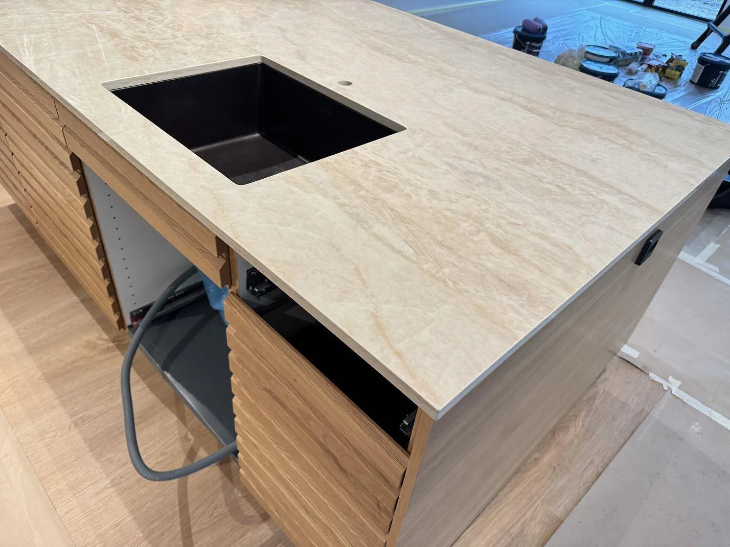 Polerad köksbänkskiva i Dekton Arga på en köksö med rektangulärt urtag, rund genomföring och öppna träluckor under montering i Köpenhamn S.