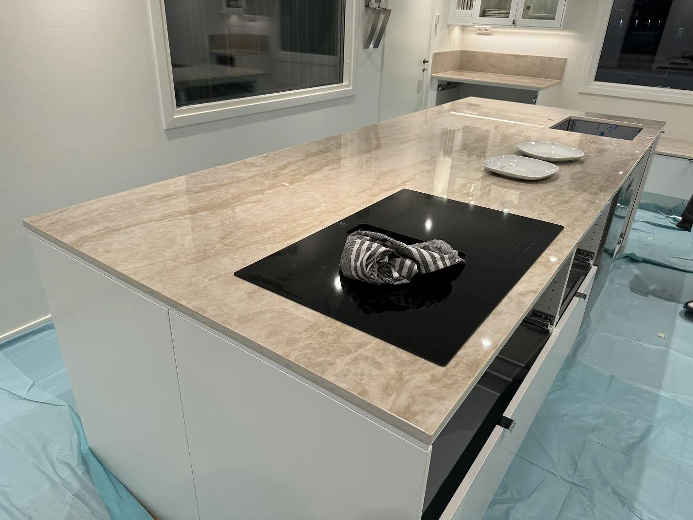 Köksö i polerad Dekton Arga med svart induktionshäll, underlimmad diskho och blått golvskydd under montering i Kristianstad.