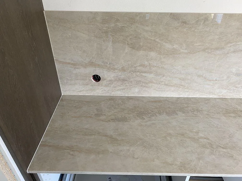 Polerad Dekton Arga keramik som bänkskiva och väggbeklädnad med synligt hål i stänkskyddet i köket i Kristianstad.