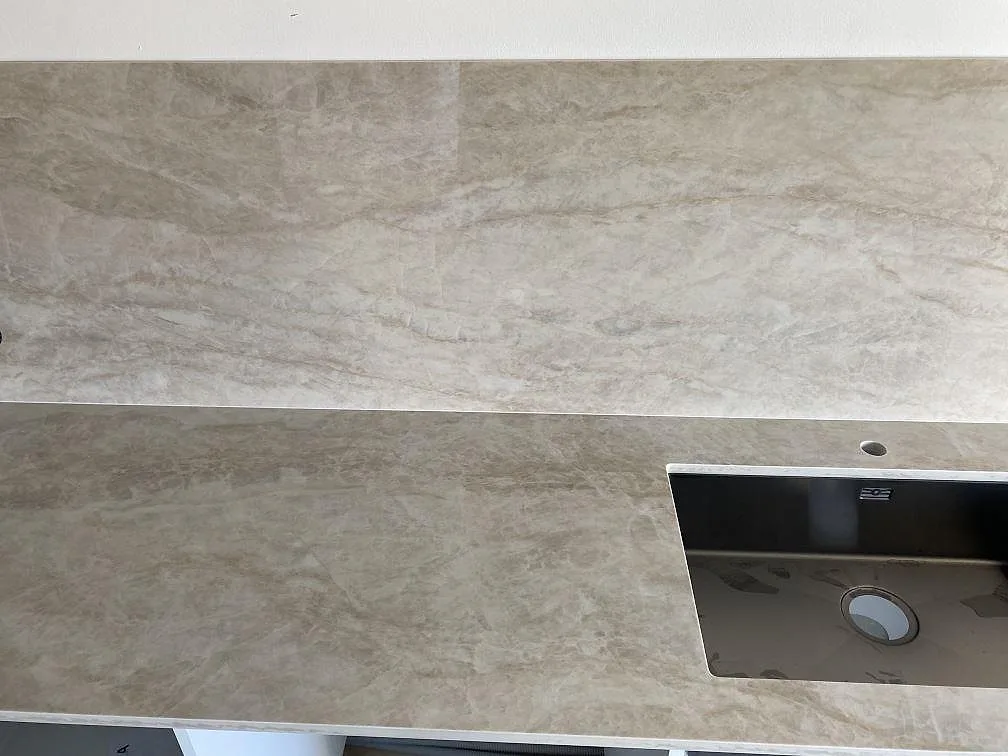 Köksbänkskiva i polerad Dekton Arga med svart diskho, blandarhål och marmorerad väggbeklädnad i Kristianstad.