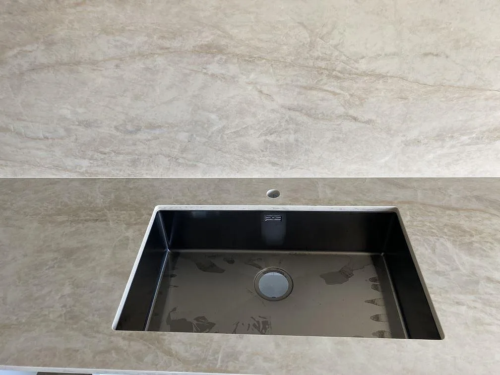 Närbild på svart diskho monterad i polerad Dekton Arga keramik med matchande väggbeklädnad i ett kök i Kristianstad.
