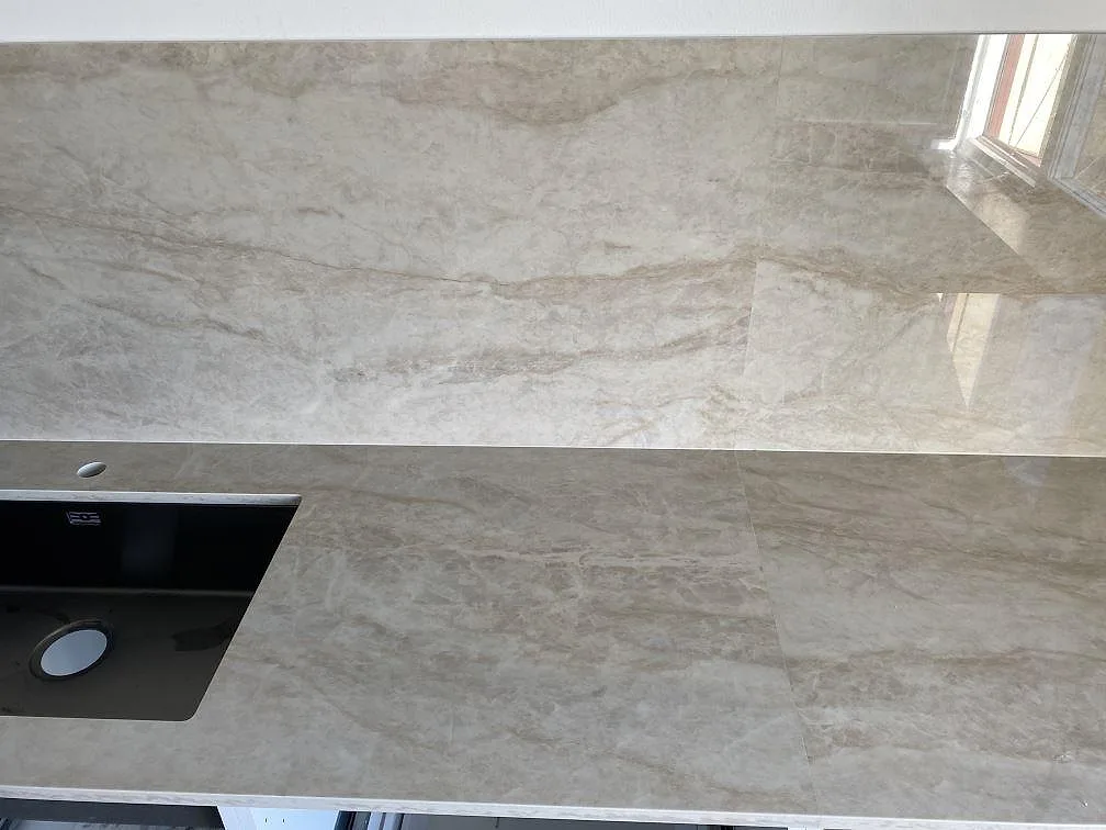 Polerad Dekton Arga köksbänkskiva med synlig svart diskho, ljus ådring och reflekterande väggpanel i Kristianstad.
