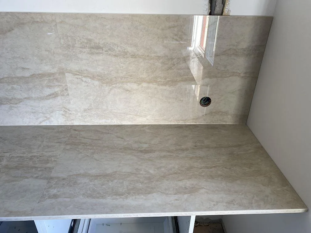 Höger bänkyta i polerad Dekton Arga keramik med hög väggbeklädnad, marmorerad struktur och rund öppning i Kristianstad.