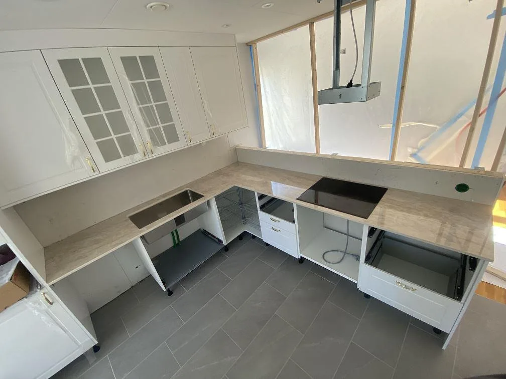 Översikt av L-format kök i Landvetter med köksbänkskiva i Dekton Arga, underlimmad rostfri diskho och induktionshäll, fotat under montering.
