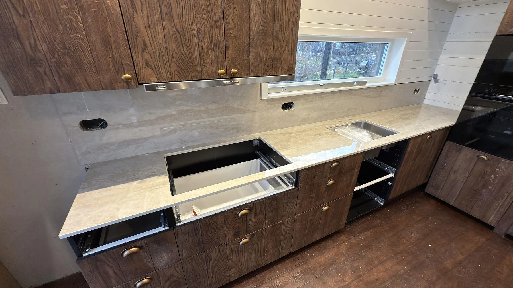 Köksbänkskiva i polerad Dekton Arga, ljus keramik, med väggbeklädnad i samma sten och öppen hällurtagning i ett kök under montering i Lidingö.