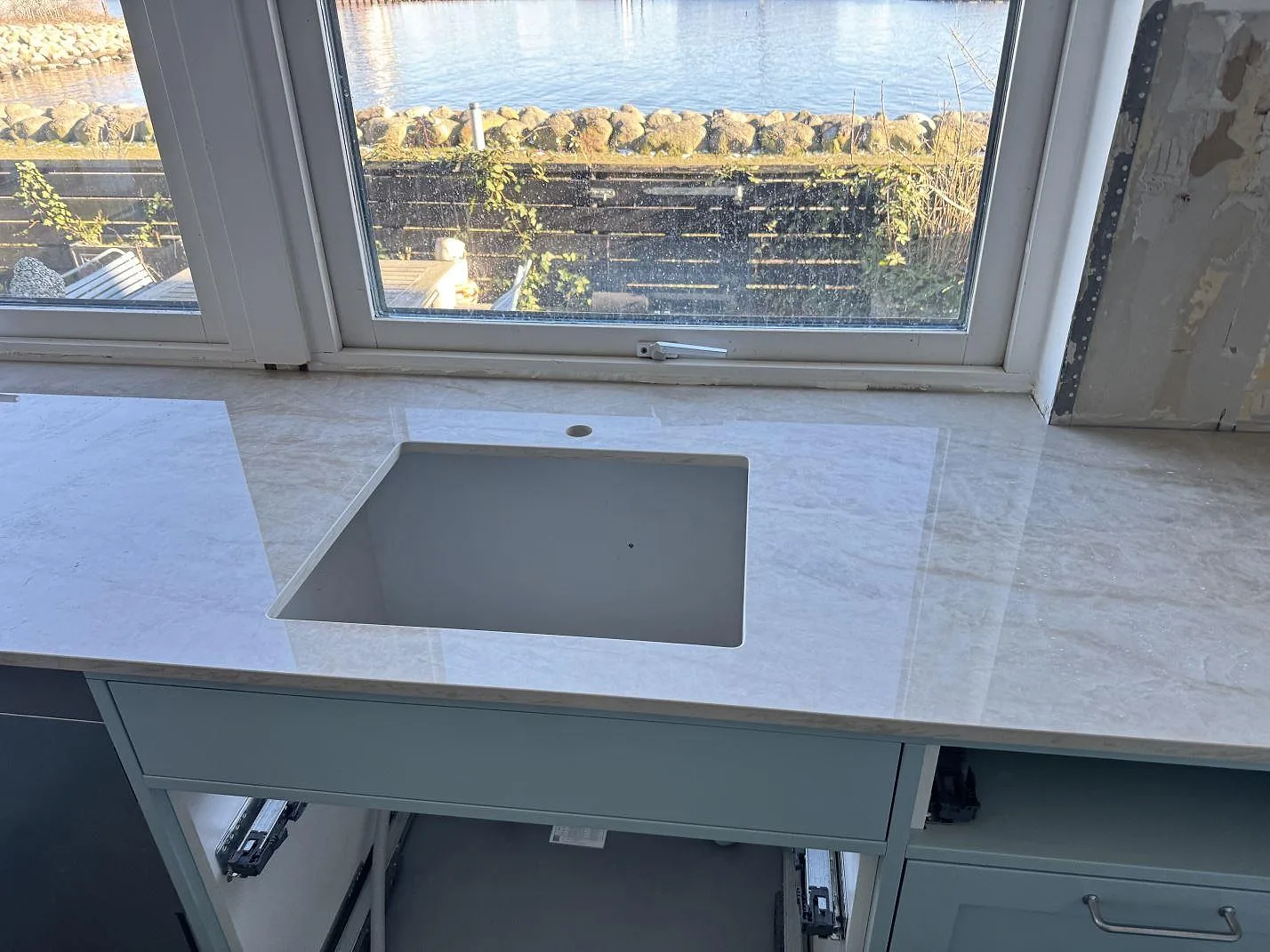 Polerad Dekton Arga som köksbänkskiva under fönster, med öppet urtag och ljus marmorerad ådring i Limhamn.