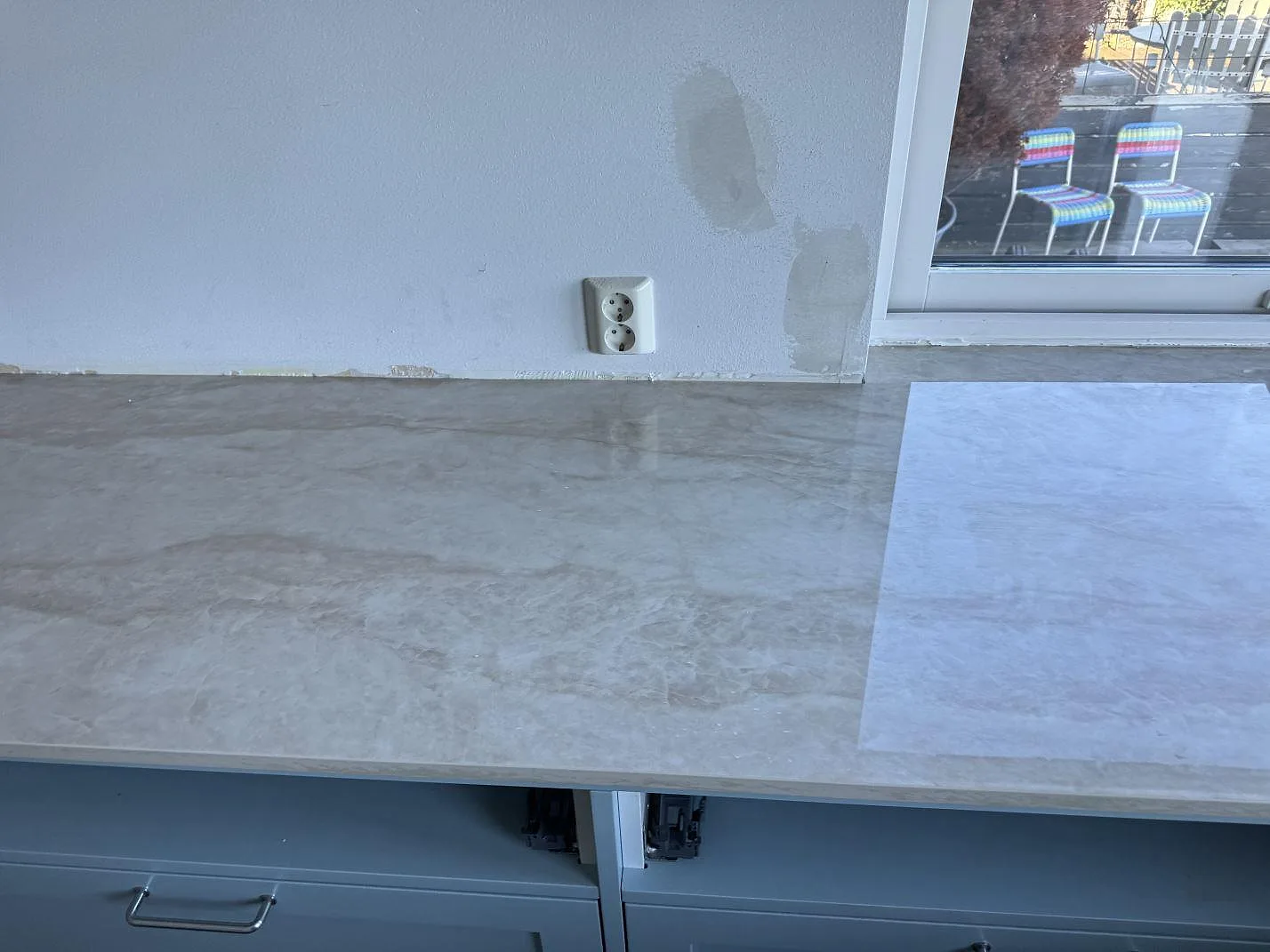 Rak köksbänkskiva i polerad Dekton Arga, keramik, på ljusblå stommar mot vit vägg i Limhamn.
