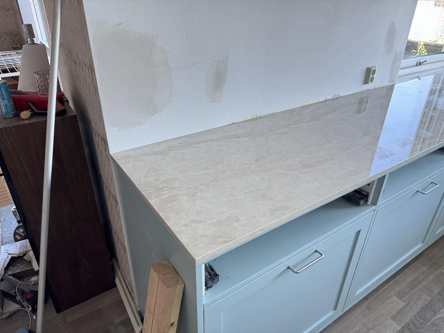 Lång bänkdel i polerad Dekton Arga med ljus marmorering på köksstommar under montering i Limhamn.