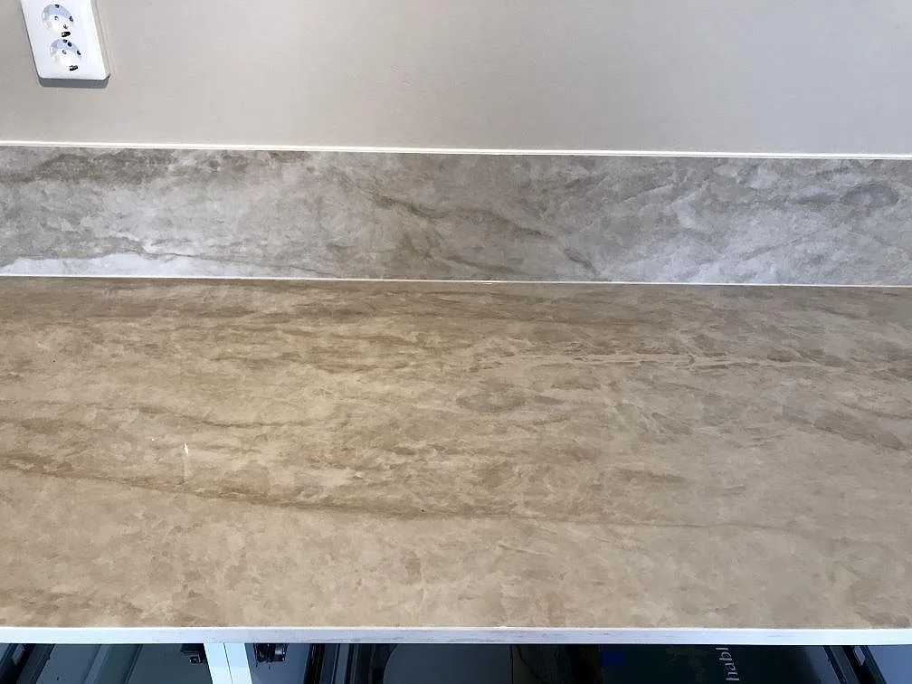 Polerad Dekton Arga köksbänkskiva med brun-guldig ådring och uppvikt stänkkant längs väggen i Lomma.