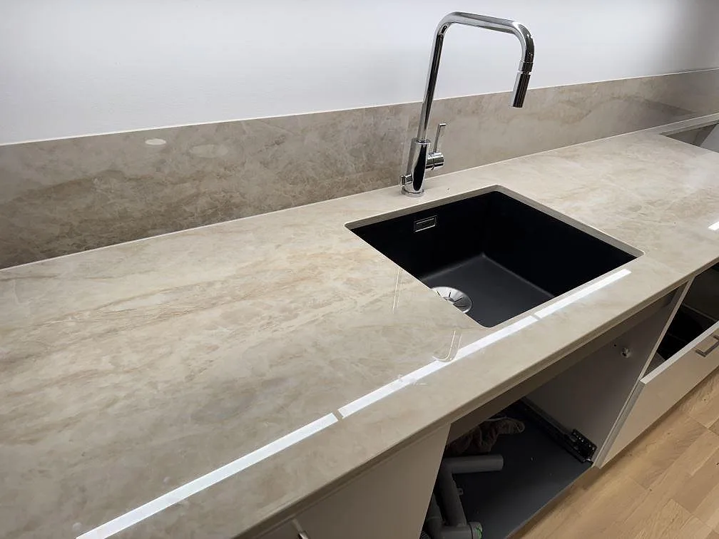 Polerad köksbänkskiva i Dekton Arga keramik med svart diskho, hög blandare och uppvikt stänkskydd i ett kök i Lomma.