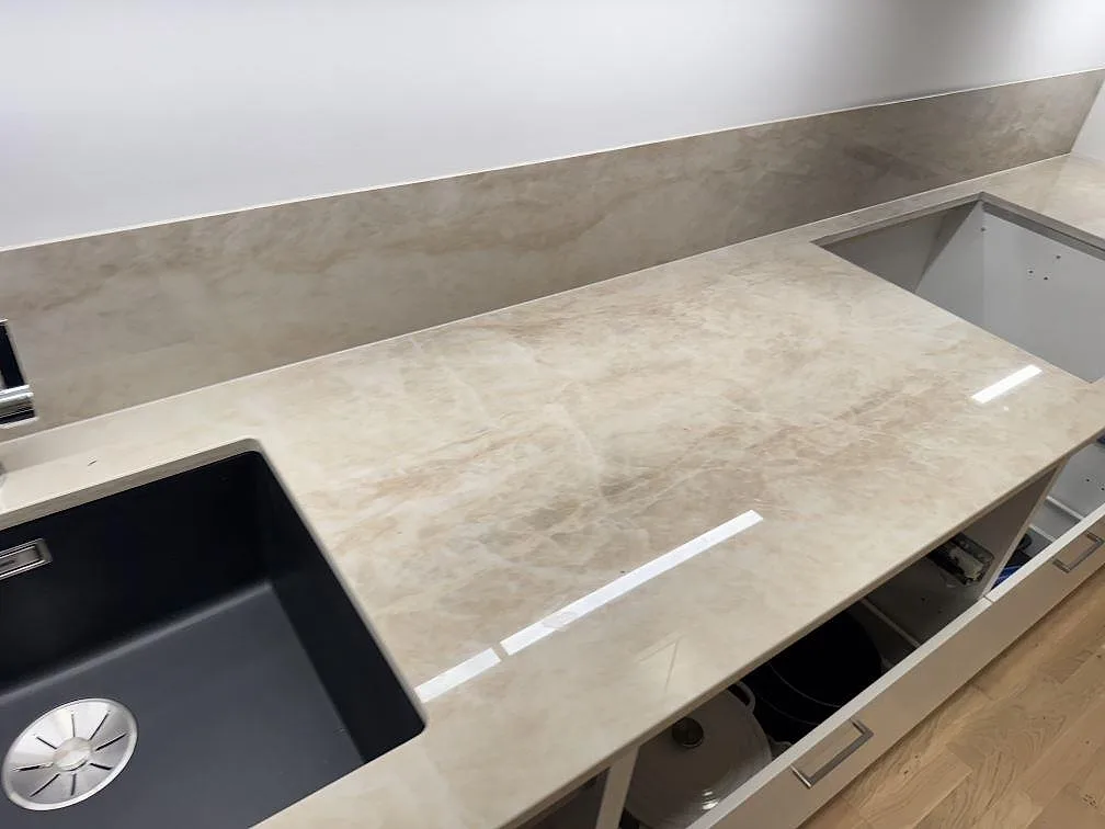 Lång arbetsyta i polerad Dekton Arga keramik med svart diskho, hälluttag och matchande stänkskydd i ett kök i Lomma.