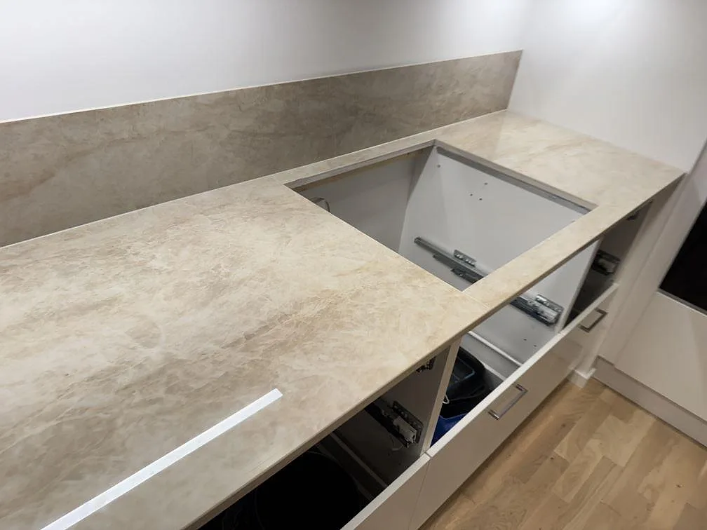 Höger bänkdel i polerad Dekton Arga keramik med öppet hälluttag, stänkskydd och ljusa köksstommar i Lomma.