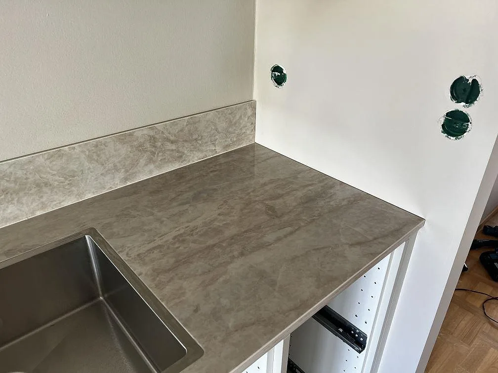 Detalj av polerad Dekton Arga bänkskiva vid diskhon med matchande stänkskydd och öppna vita köksstommar i Lund.