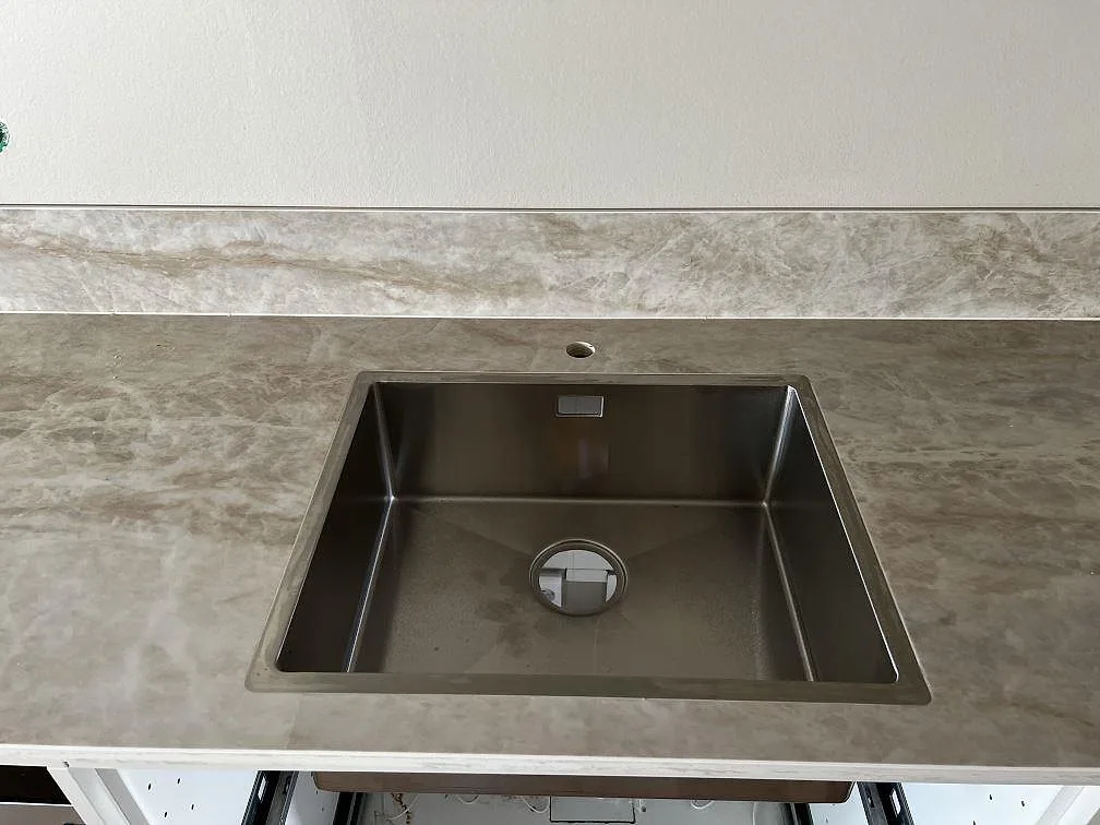 Närbild på rostfri diskho monterad under polerad Dekton Arga keramik med låg stänkkant i ett kök i Lund.
