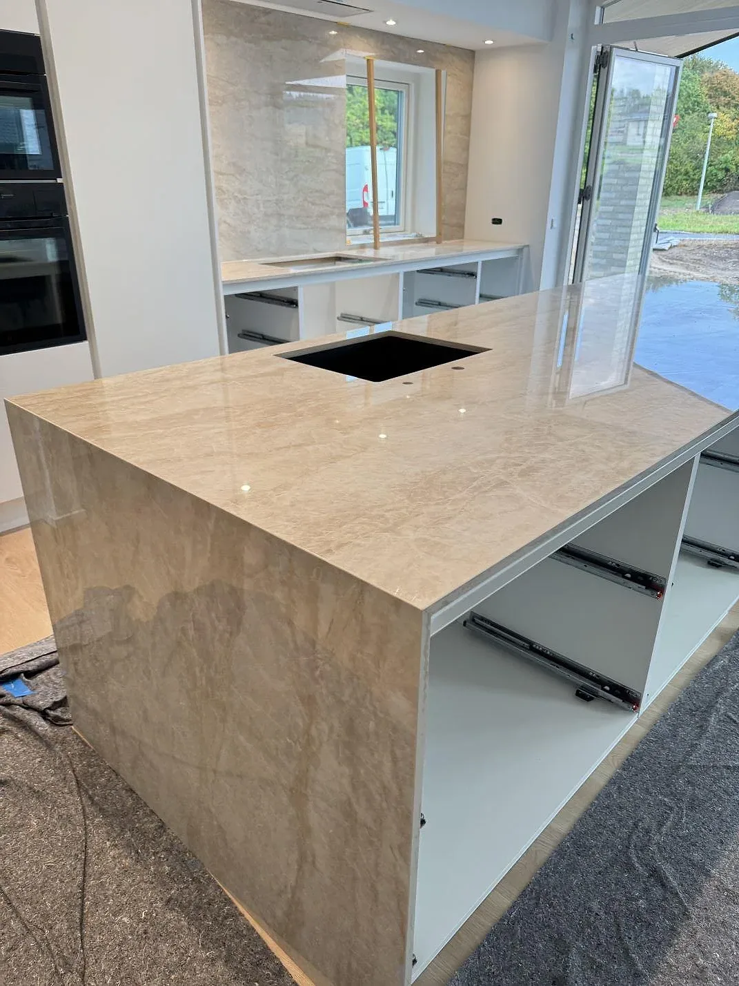 Polerad köksbänkskiva i Dekton Arga keramik med köksö, svart diskho, fallande sida och bakre väggbeklädnad i Malling.