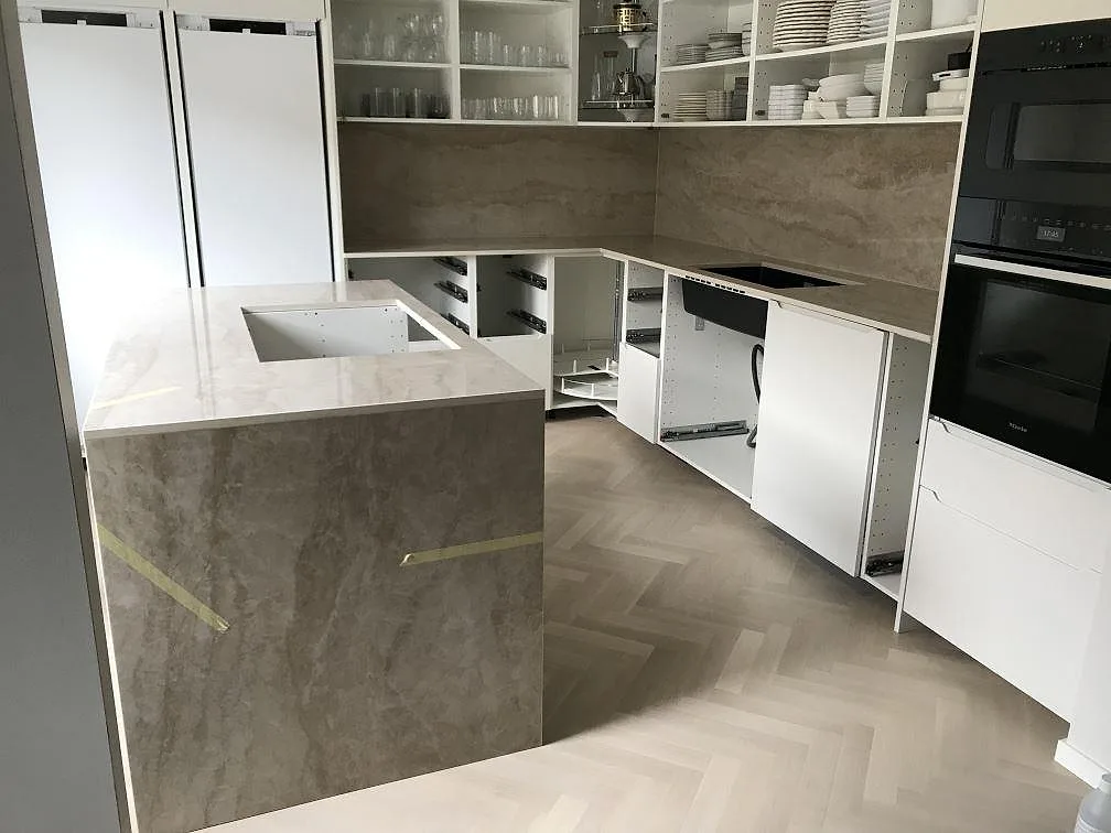 Köksbänkskiva i Dekton Arga, polerad keramik i marmorlook, i ett U-format kök med köksö och heltäckande stänkskydd i samma sten i Malmö.