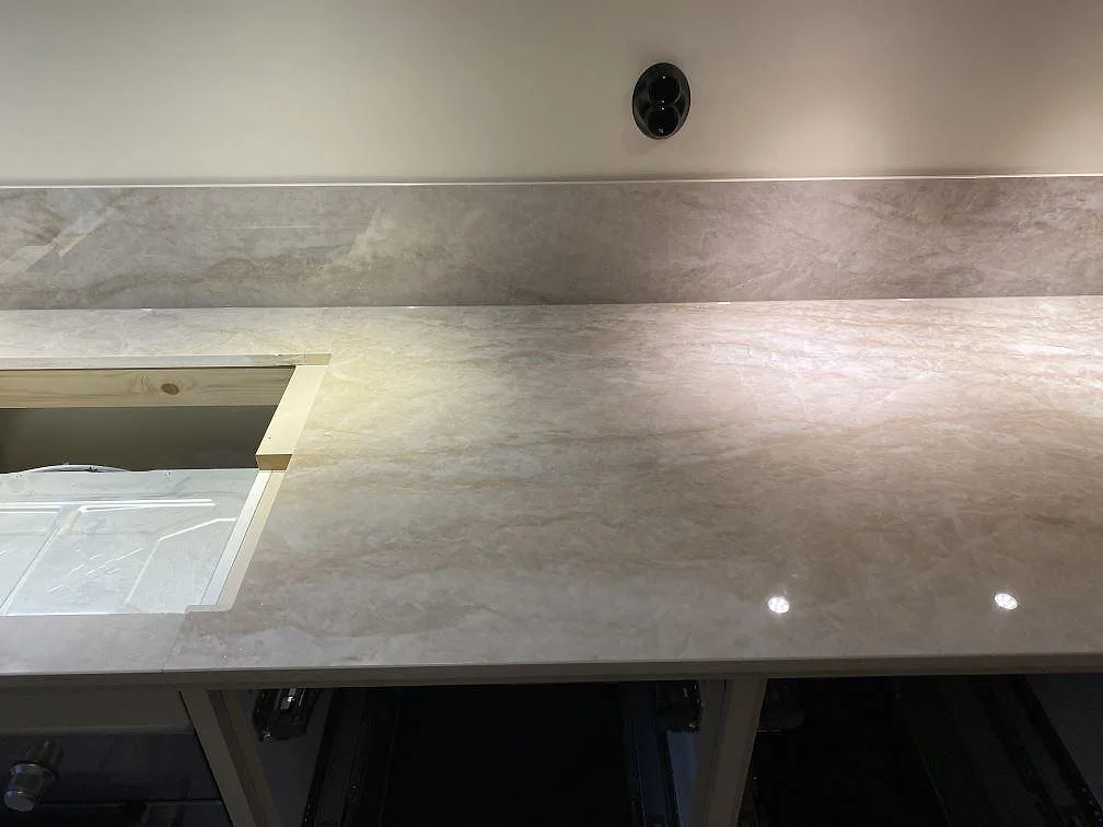 Närbild av polerad Dekton Arga köksbänkskiva med ljus ådring, stänkskydd och hällurtag under montering i Malmö.