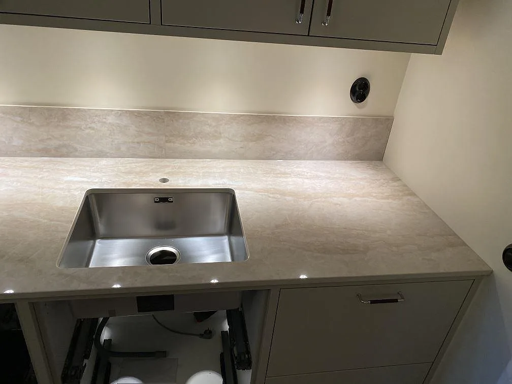 Höger del av köksbänkskiva i Dekton Arga keramik med rostfri diskho, grå skåp och låg stänkkant i Malmö.
