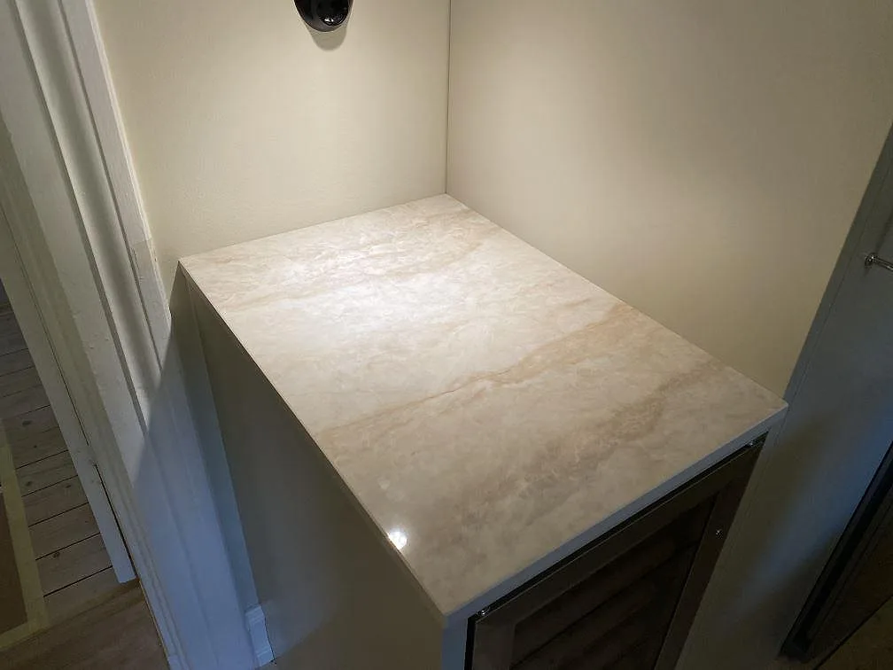 Sidobänk i polerad Dekton Arga keramik med krämfärgad ådring monterad vid vägg i Malmö.