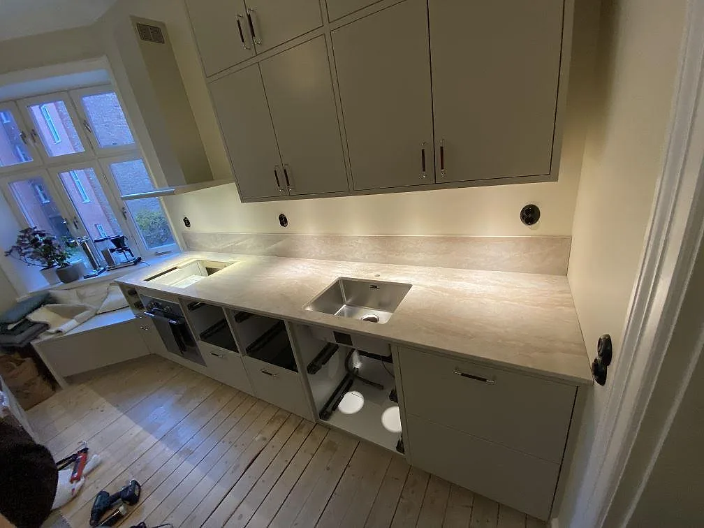 Köksbänkskiva i polerad Dekton Arga keramik med låg stänkkant längs en köksvägg under montering i Malmö.