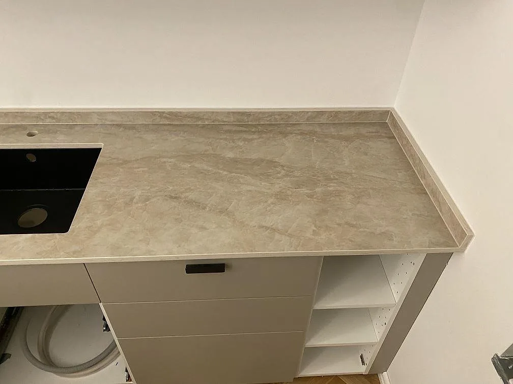 Köksbänkskiva i varmt gräddvit Dekton Arga keramik, polerad, med underlimmad svart diskho och låga skåp i ett kök i Malmö.