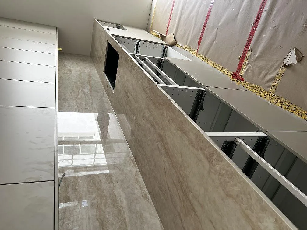 Köksbänkskiva i ljust gråmelerad Dekton Arga, polerad, med matchande väggbeklädnad i ett halvfärdigt kök i Malmö.
