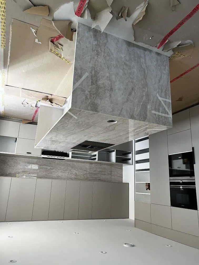 Köksö med vattenfallskant i polerad Dekton Arga och infälld induktionshäll i ett kök under montering i Malmö.