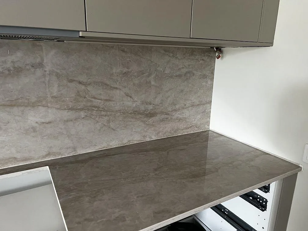 Höger del av L-formad köksbänkskiva i polerad Dekton Arga med stänkskydd och grå köksstommar i Malmö.