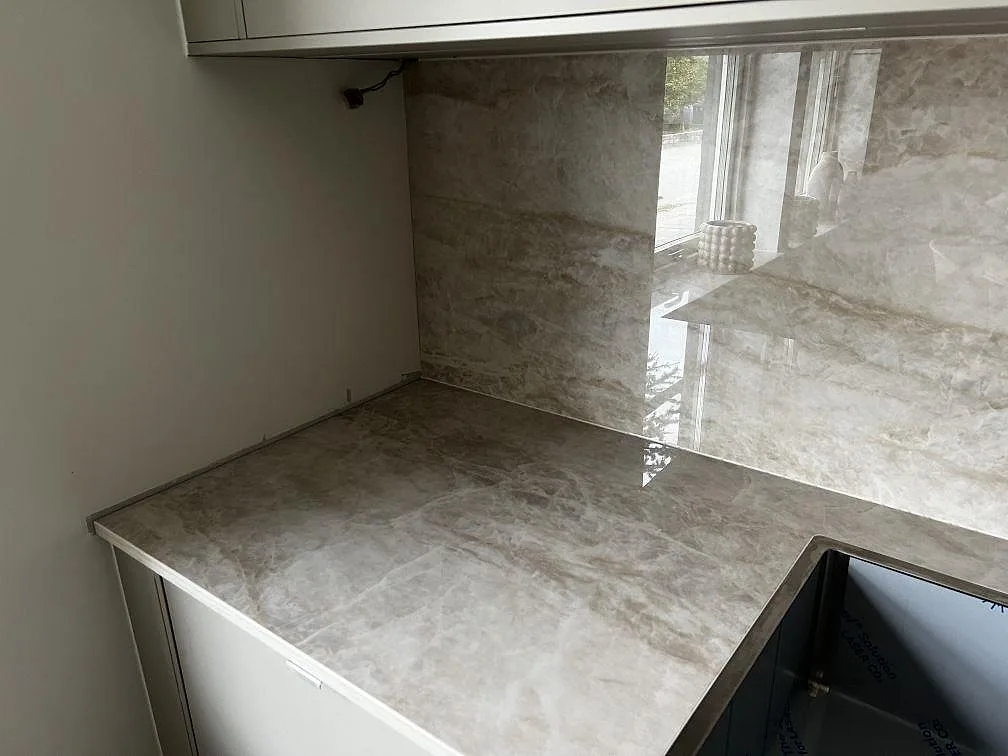 Vänster hörn av köksbänkskiva i polerad Dekton Arga intill svart diskho och stänkskydd i Malmö.