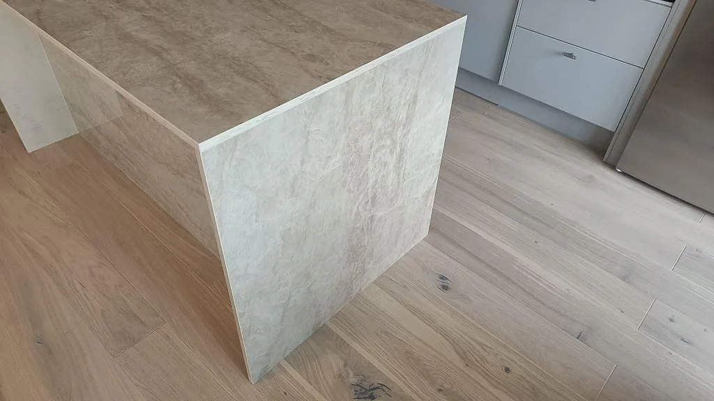 Gavel på köksö i polerad keramisk Dekton Arga där stenen fortsätter ned mot trägolvet i Malmö.