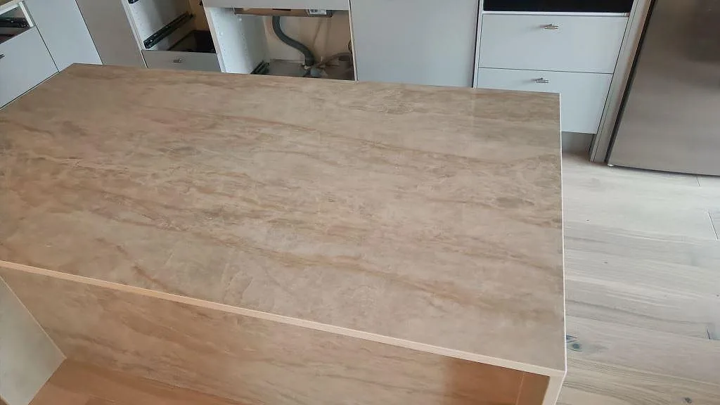 Toppskiva på köksö i polerad keramisk Dekton Arga med marmorerad ådring under montering i Malmö.
