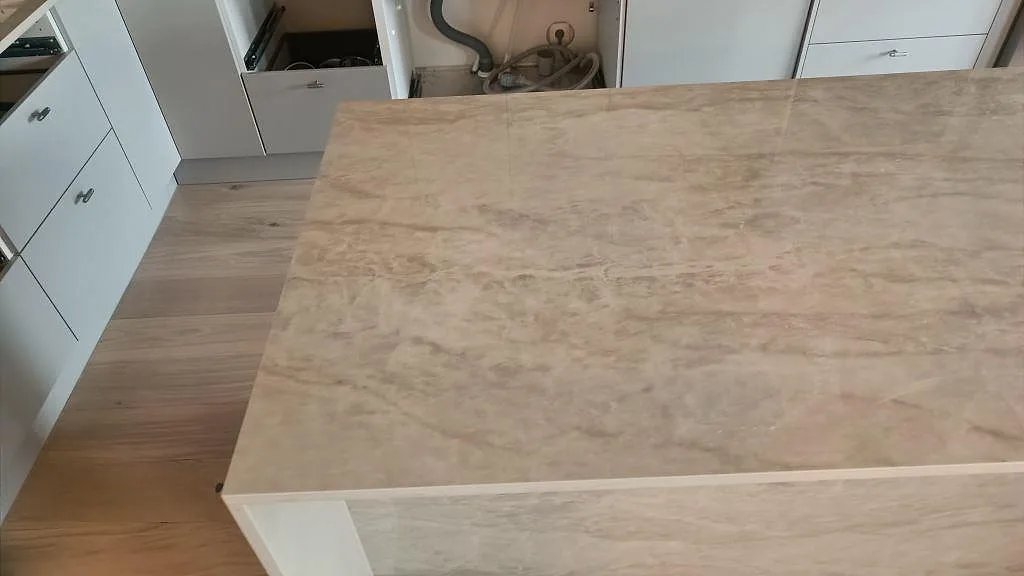 Detalj av den polerade keramiska Dekton Arga ytan på köksön framför öppna köksstommar i Malmö.