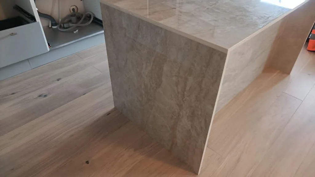 Sidovy av köksö i polerad keramisk Dekton Arga med sammanhängande skiva och vattenfallssida i Malmö.