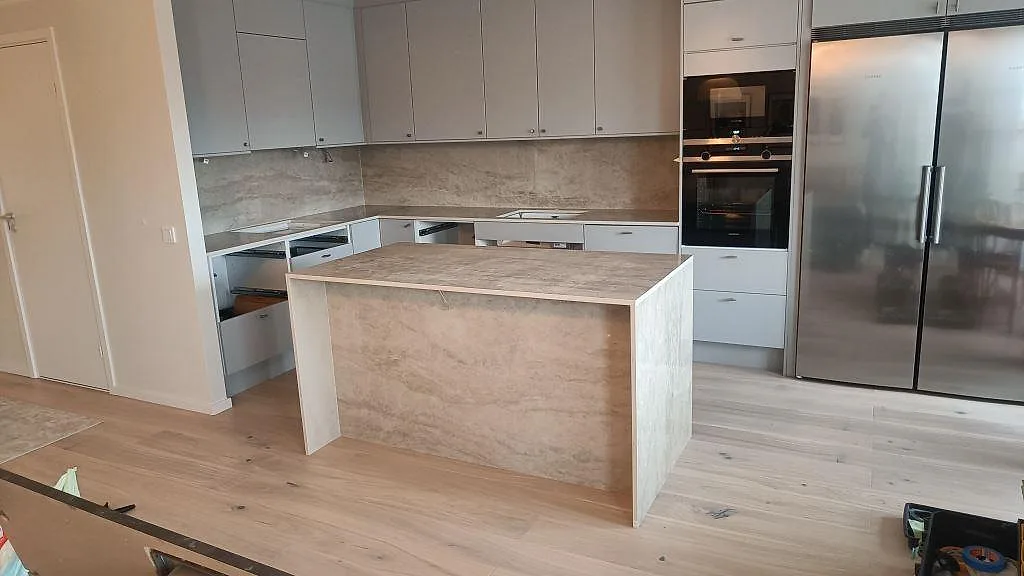 Keramisk köksbänkskiva i polerad Dekton Arga med vattenfallsklädd köksö, perimeterbänkar och stänkskydd i ett kök i Malmö.