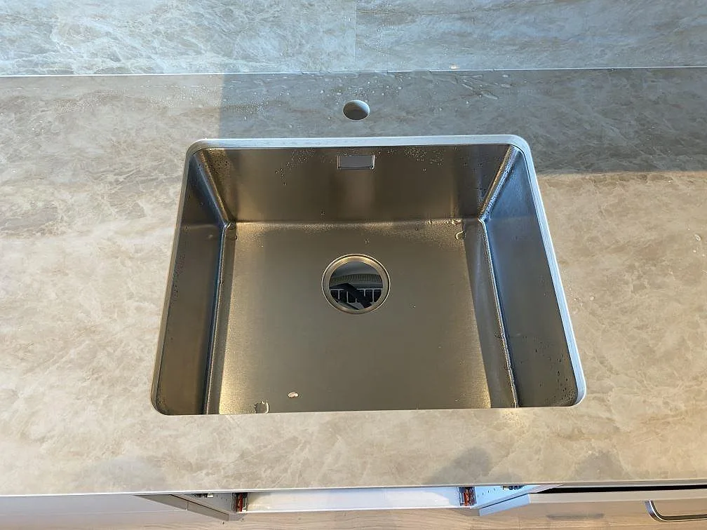 Närbild på diskho i polerad Dekton Arga med matchande stänkskydd och ljus ådring i ett Malmö-kök.