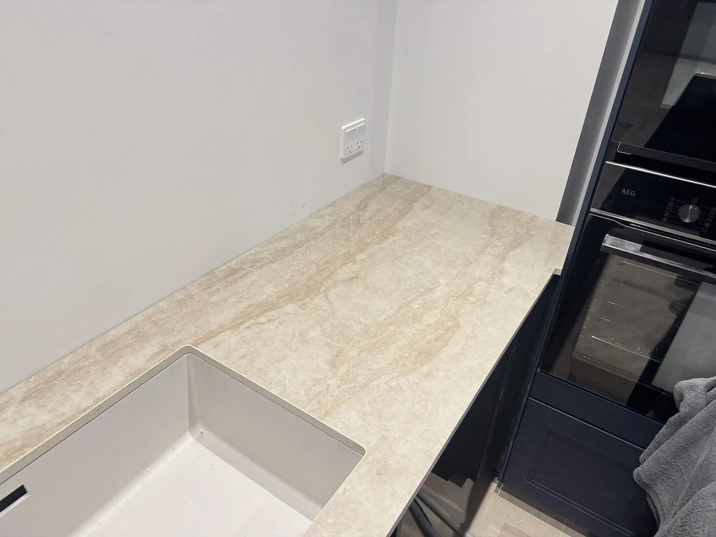 Polerad Dekton Arga köksbänkskiva som löper fram till höga AEG-inbyggnadsugnar med vit underlimmad diskho i ett kök i Marstal på Ærø.
