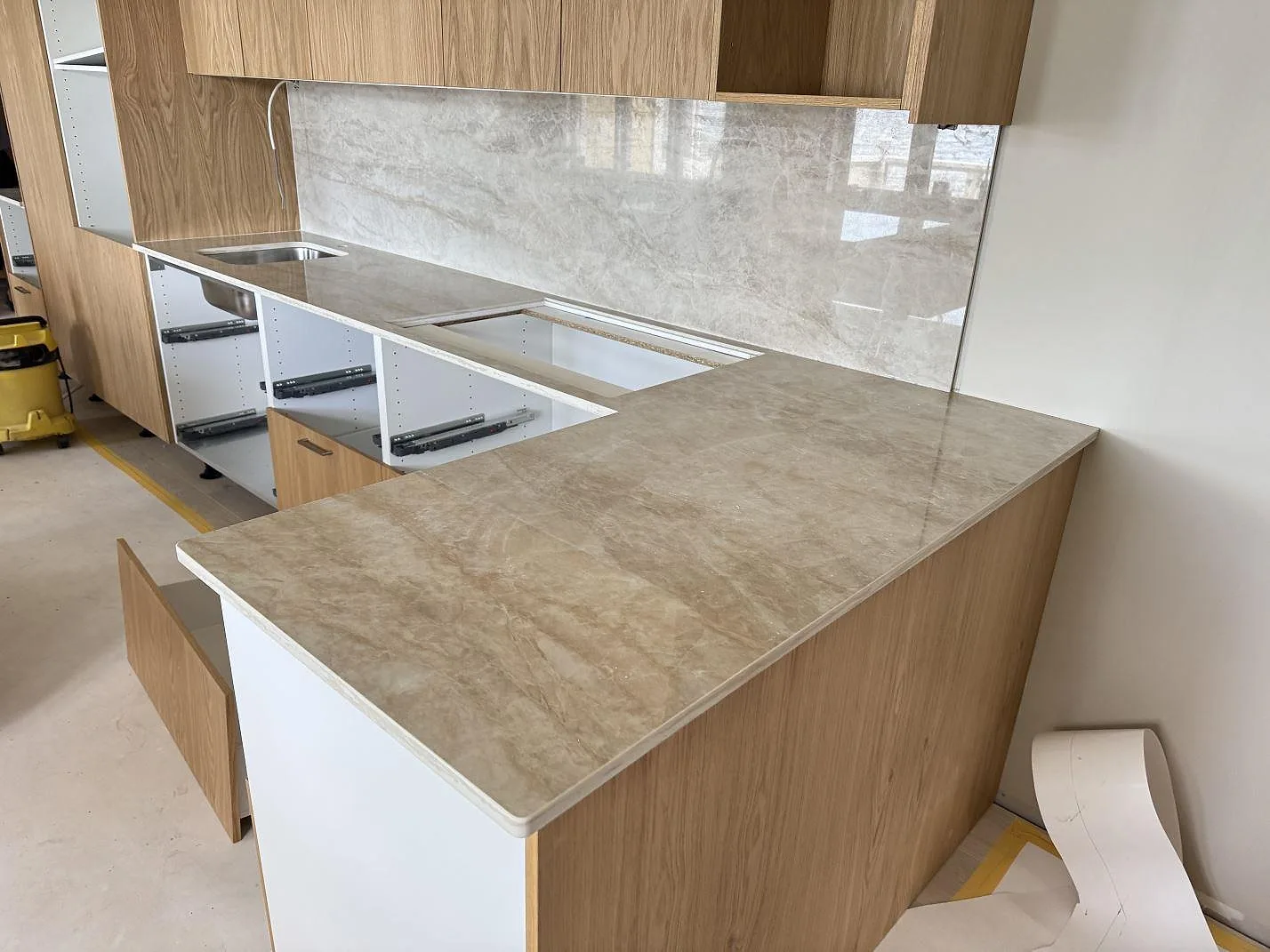 Köksbänkskiva i polerad Dekton Arga med stänkskydd, hällurtag och rostfri diskho i ett kök i Mölltorp under montering.