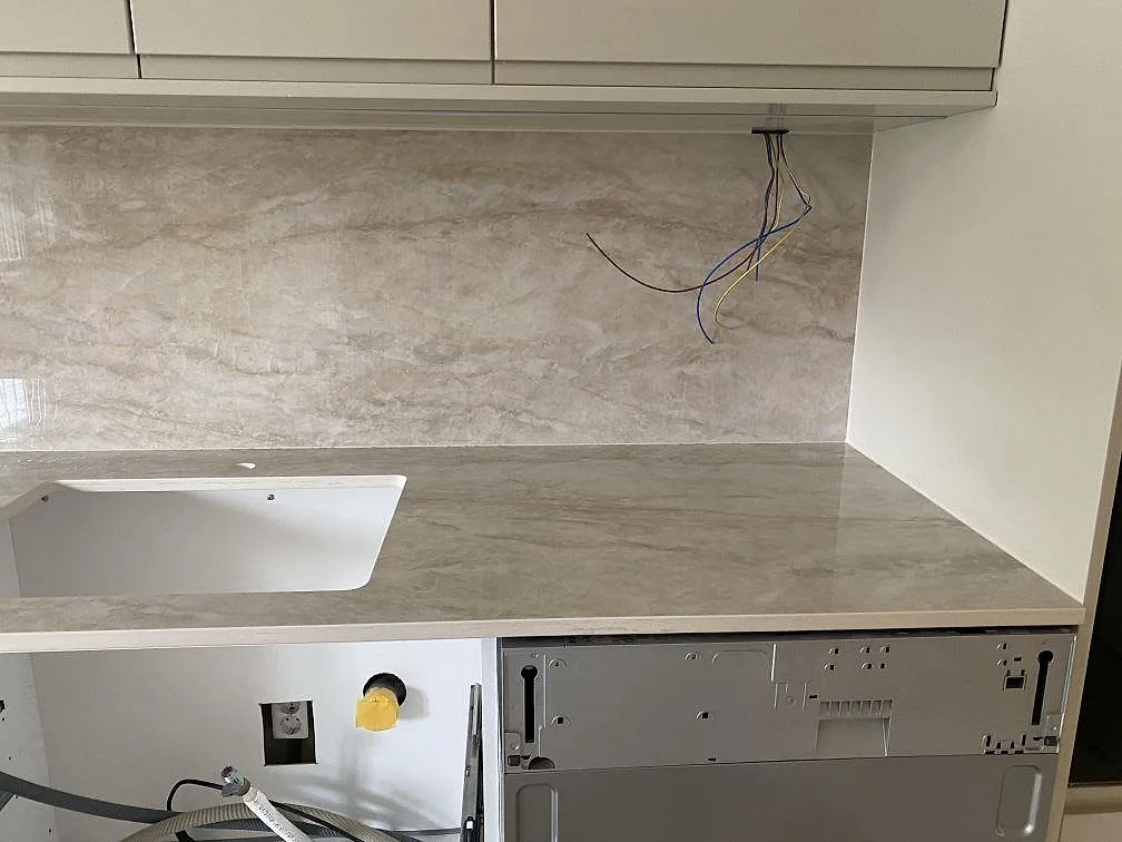 Polerad köksbänkskiva i Dekton Arga keramik med blankt stänkskydd och öppna underskåp under montering i Mölndal.