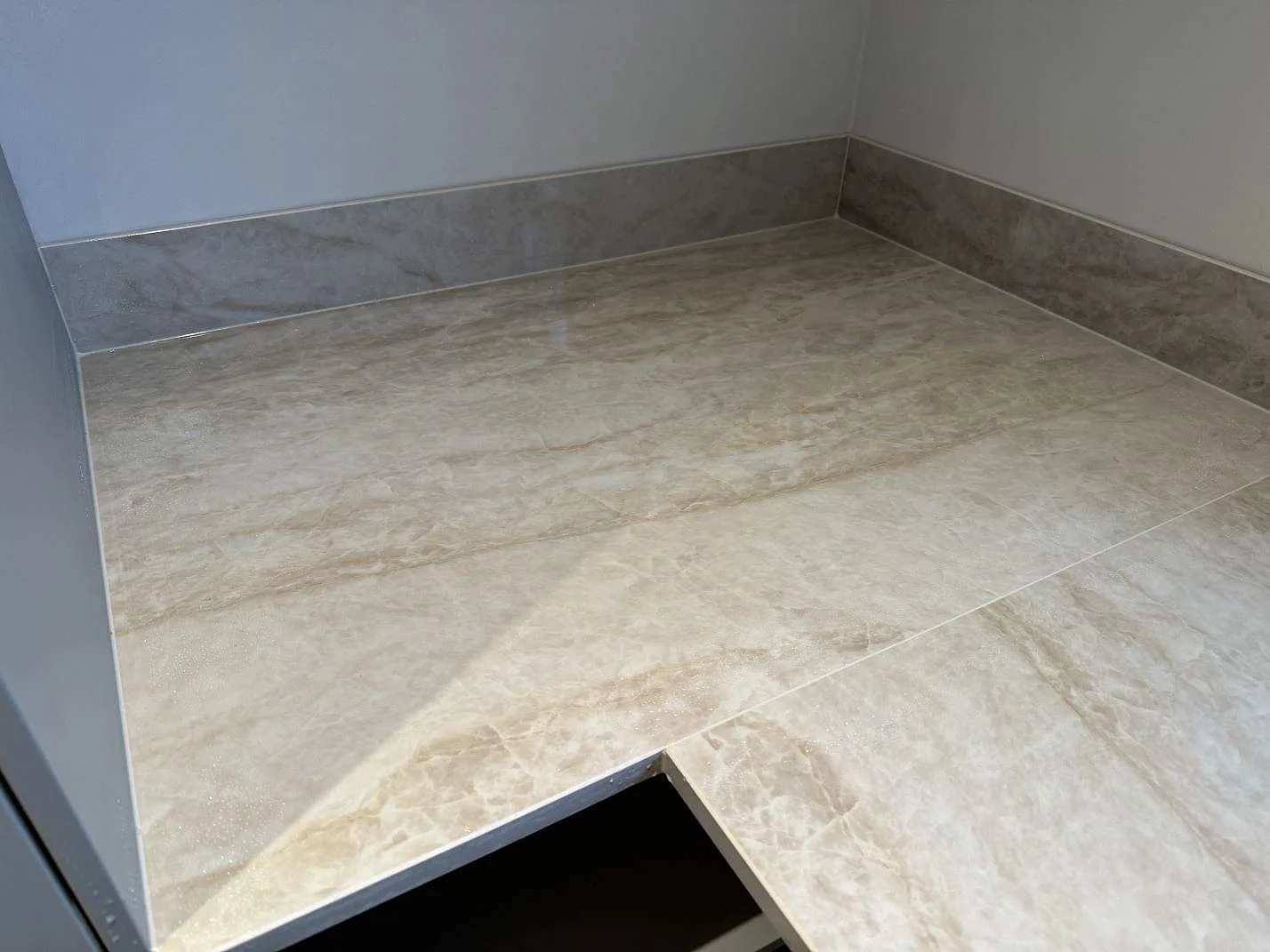 Hörnvy av L-formad köksbänkskiva i polerad Dekton Arga med uppvikt stänkkant och vit köksstomme i Mölndal.