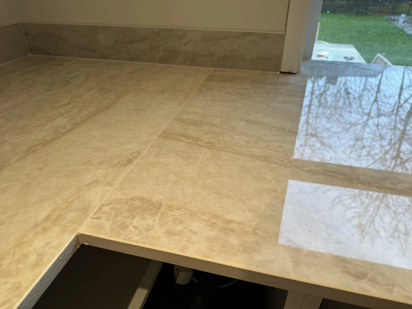 Blankpolerad Dekton Arga bänkskiva med fönsterreflektion, beige ådring och lågt stänkskydd i Mölndal.