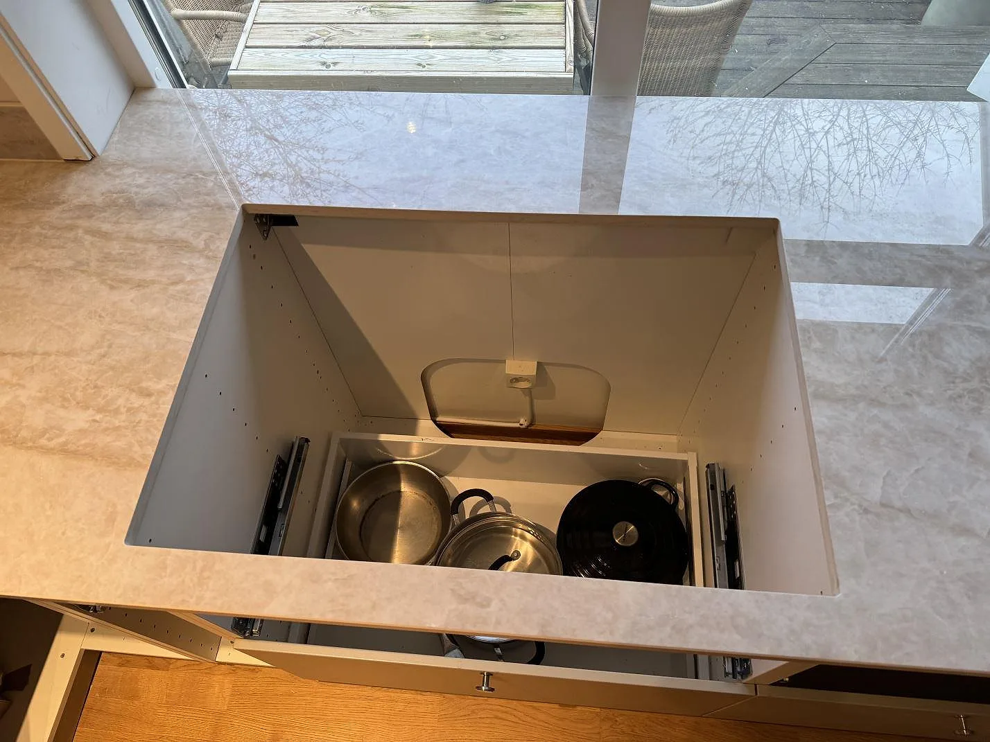 Detalj av polerad Dekton Arga runt en utdragen låda, med ljus stenådring och stora fönster i köket i Mölndal.