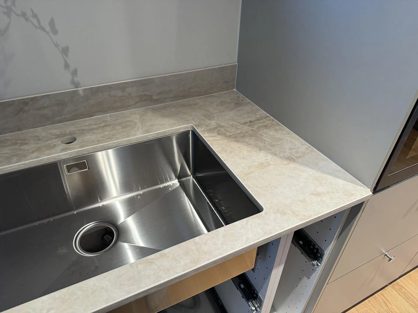 Underlimmad rostfri diskho i en polerad Dekton Arga bänkskiva med matchande stänkskydd i ett kök i Mölndal.